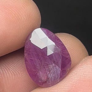 May include: A deep pink, faceted gemstone with a teardrop shape.