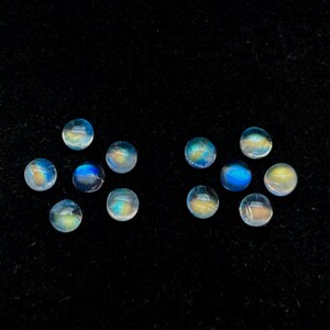 May include: Twelve round, iridescent moonstone cabochons in various shades of blue and white, arranged in two rows on a black velvet background.