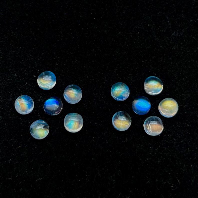 May include: Twelve round, iridescent moonstone cabochons in various shades of blue and white, arranged in two rows on a black velvet background.