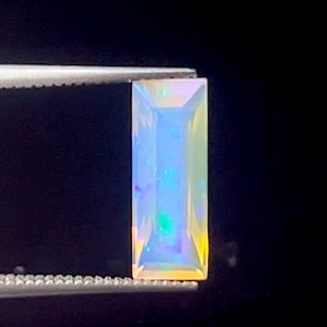 May include: A rectangular, iridescent opal gemstone with a light blue, green, and yellow color.