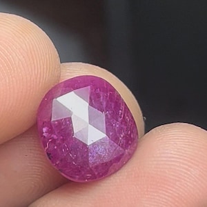 May include: A deep pink ruby gemstone with a faceted cut. The gemstone is oval shaped and has a high polish.