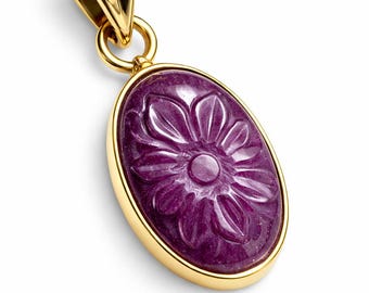 Könnte beinhalten: Ovaler Anhänger mit einem geschnitzten, lila Edelstein-Blumendesign, gefasst in einem goldfarbenen Rahmen. Der Anhänger hat eine goldfarbene Öse zum Befestigen an einer Kette. Der Edelstein ist tiefviolett.