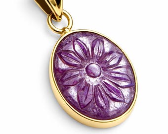 Könnte beinhalten: Goldener Anhänger mit einem ovalen, geschnitzten lila Edelstein. Der Edelstein hat ein Blumenmuster. Der Anhänger hat eine goldene Öse und einen goldenen Rahmen. Der Hintergrund ist weiß.