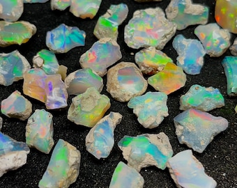 May include: A collection of rough opal stones with iridescent colors, including green, blue, and purple. The stones are various sizes and shapes, and some have a rough, natural texture.