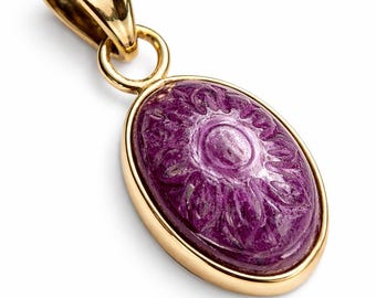 Könnte beinhalten: Goldener Anhänger mit einem ovalen, geschnitzten, lila Edelstein. Der Edelstein hat ein Blumenmuster. Der Anhänger hat eine goldene Öse und einen goldenen Rahmen.