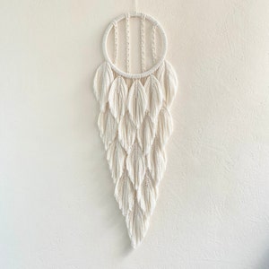 May include: A white macrame wall hanging with a circular top and a cascading design of fringe tassels.