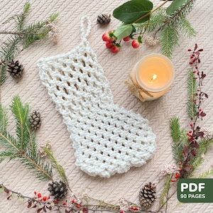May include: A handmade, off-white crochet Christmas stocking with a loop for hanging. The stocking is surrounded by pine branches, berries, and pine cones. A lit candle in a glass jar is also present. The image includes the text "PDF 90 pages".