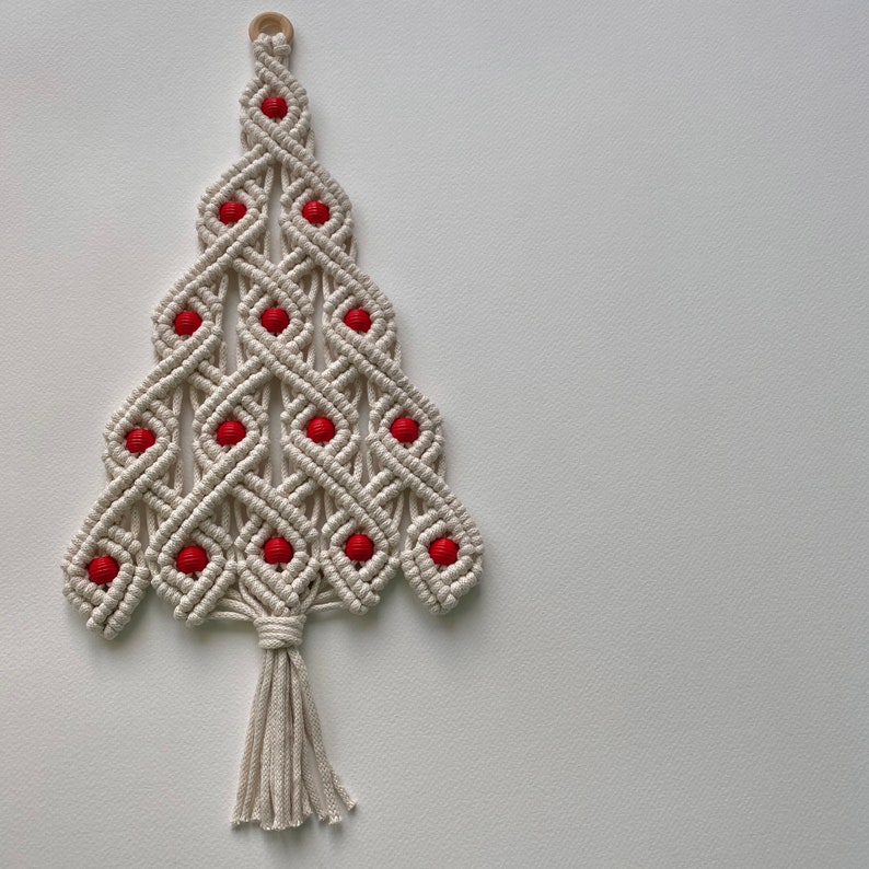 May include: A white macrame Christmas tree wall hanging with red beads. The tree has a tassel at the bottom.