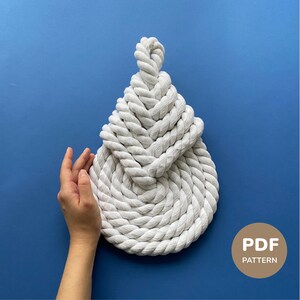 May include: A white rope knot, possibly a coaster or decorative item, against a blue background. The rope is tightly woven, forming a circular shape with a looped top. The image includes a "PDF PATTERN" label.
