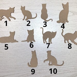 May include: A selection of ten cat-shaped cutouts in various poses. The cutouts are made of a light brown material and are numbered from one to ten. The cats are in different positions, including sitting, standing, and lying down.