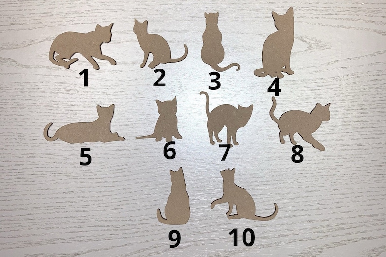 May include: A selection of ten cat-shaped cutouts in various poses. The cutouts are made of a light brown material and are numbered from one to ten. The cats are in different positions, including sitting, standing, and lying down.