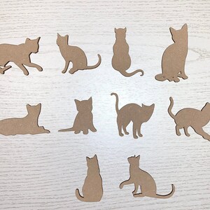 May include: Eleven cat silhouettes in different poses, cut from light brown material. The cats are shown sitting, standing, and walking, with their tails and ears clearly defined. The shapes are arranged on a light wood-grain surface.