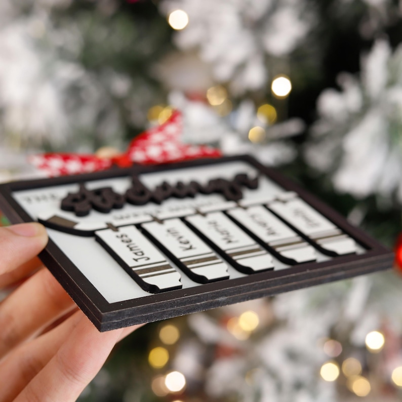 May include: A white wooden Christmas ornament with the text "The Christmas" and five crayon-shaped name tags with the names "James", "Kevin", "Molly", "Sarah", and "Greg".