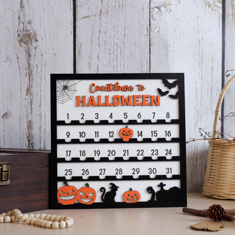 May include: A black framed Halloween countdown calendar with the words "Countdown to Halloween" in orange. The calendar features numbers, pumpkins, bats, a spiderweb, and a black cat silhouette.