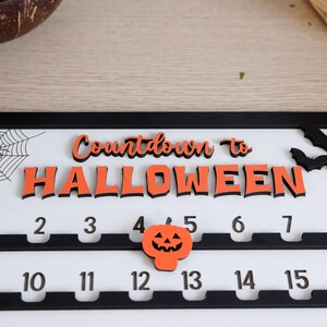 May include: A Halloween countdown calendar with the words "Countdown to Halloween" in orange and black. The calendar has numbers 2-7 and 10-15, with a pumpkin icon. A spiderweb and bats are also visible.