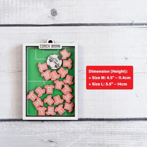 Pode incluir: Um quadro de exibi&ccedil;&atilde;o de madeira com tema de futebol com um design de campo verde. Apresenta uma bola de futebol e pequenas pe&ccedil;as rosa em forma de camisa com n&uacute;meros. O texto "COACH BRIAN" est&aacute; no topo. O tamanho M tem 11,4 cm de altura e o tamanho L tem 14 cm de altura.