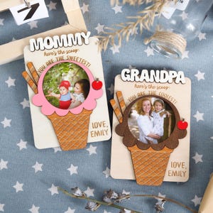 May include: Two wooden photo frames shaped like ice cream cones. The frames have a pink and brown ice cream cone design with a photo insert. The frames have the text "Mommy here's the scoop: You are the sweetest! Love, Emily" and "Grandpa here's the scoop: You are the coolest! Love, Emily".
