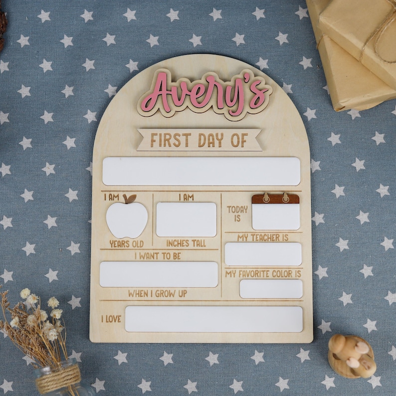 May include: Wooden first day of school sign with the name "Avery's" in pink. The sign has spaces to fill in information about the child's first day, including age, height, teacher, and favorite color.