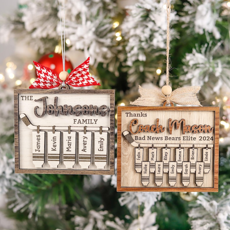 May include: Two wooden Christmas decorations featuring hockey stick designs. The top ornament reads "The Johnsons Family" with names on each stick. The bottom ornament reads "Thanks Coach Macon Bad News Bears Elite 2024" with names on each stick.