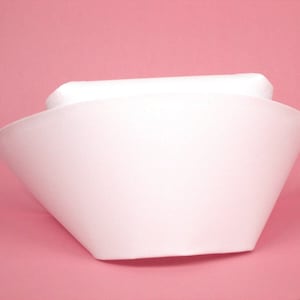 May include: A white nurse's cap with a wide brim and a flat top. The cap is made of a smooth, white fabric.