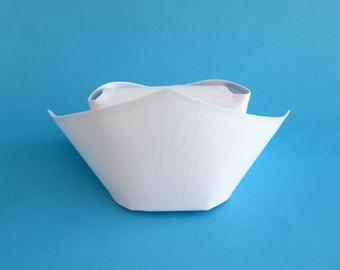 May include: A white nurse's cap with a pointed top and a wide brim. The cap is made of a smooth, white fabric.