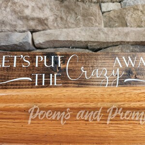 May include: A wooden sign with the text "Let's Put The Crazy Away" in white lettering on a dark brown background.