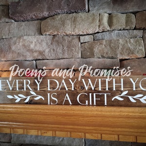 May include: A wooden sign with the text "Poems and Promises Every Day With You Is A Gift" in white lettering. The sign is on a wooden mantel with a decorative reindeer figurine.