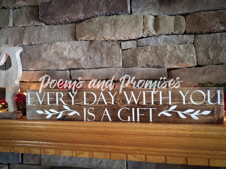 May include: A wooden sign with the text "Poems and Promises Every Day With You Is A Gift" in white lettering. The sign is on a wooden mantel with a decorative reindeer figurine.