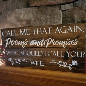 May include: A wooden sign with the text "CALL ME THAT AGAIN. Poems and Promises WHAT SHOULD I CALL YOU? WIFE." in white lettering. The sign has a rustic brown finish and is decorated with white floral designs.