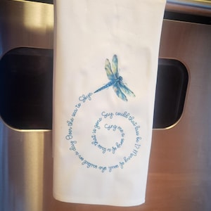 Puede incluir: Una toalla de cocina blanca con un diseño de libélula azul y una cita en texto azul que dice: "Si una chica para llamar a tass es 1? Alegre del alma del día Sobre el mar a Skye. Di Ging me que se ha ido llamado en un",