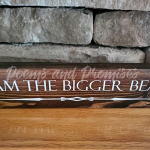 May include: A dark brown wooden sign with the text "I AM THE BIGGER BEAR" in white lettering. The sign has a decorative design at the bottom.