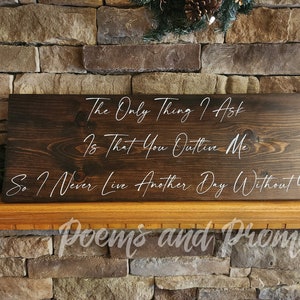 May include: A dark brown wooden sign with white lettering that reads "The Only Thing I Ask Is That You Outlive Me So I Never Live Another Day Without You". The sign is sitting on a stone fireplace mantel.