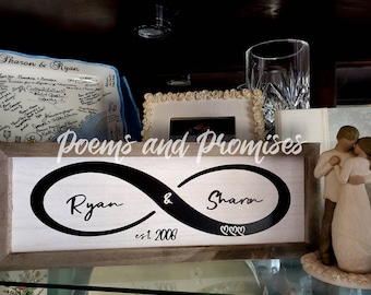 May include: A framed wooden sign with a black infinity symbol and the names "Ryan" and "Sharon" on either side. The text "est. 2008" is below the symbol. The sign is on a shelf with other decorative items.