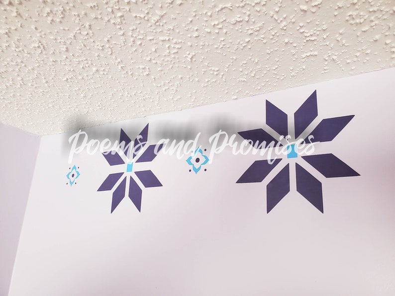 May include: A white wall with three purple and blue star-shaped wall decals. The decals are arranged in a row, with the largest decal in the center and the two smaller decals on either side. The text "Poems and Promises" is written in black cursive above the decals.