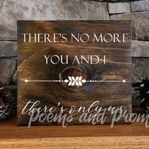 May include: A dark brown wooden sign with white text that reads "There's no more you and I there's only us poems and promises". The sign has a decorative white design in the center.