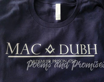 May include: A navy blue t-shirt with white text that reads "MAC DUBH" with a Masonic symbol between the words. Below the text is a white line and the words "ARDSMUIR PRISON 1753 poems and promises".