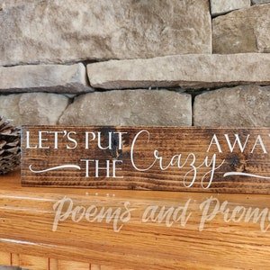May include: A rustic wooden sign with the text "Let's Put The Crazy Away" in white lettering. The sign has a dark brown stain and a distressed look.