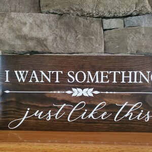 May include: A dark brown wooden sign with white text that reads "I want something just like this". The sign has a decorative arrow and leaf design.