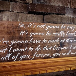 May include: A wooden sign with a white painted message that reads: "So, it's not gonna be easy. It's gonna be really hard. We're gonna have to work at this every day, but I want to do that because I want you. I want all of you, forever, you and me, every day."