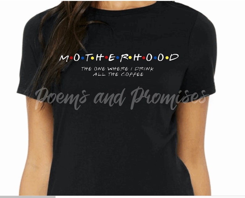 May include: Black t-shirt with the word "MOTHERHOOD" in a colorful, stylized font, with the text "THE ONE WHERE I DRINK ALL THE COFFEE" below. The shirt also has the text "Poems and Promises" in a cursive font.