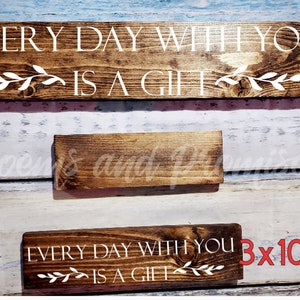May include: Two wooden signs with the text "Every day with you is a gift" in white lettering. The larger sign is 4 inches by 20 inches and the smaller sign is 3 inches by 10 inches.