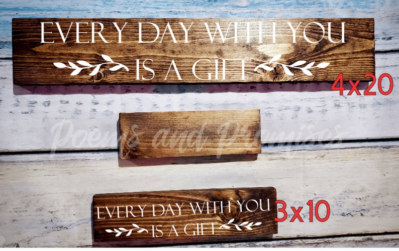 May include: Two wooden signs with the text "Every day with you is a gift" in white lettering. The larger sign is 4 inches by 20 inches and the smaller sign is 3 inches by 10 inches.