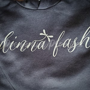 May include: A dark grey hooded sweatshirt with the text "pinna fash" in white cursive lettering and a dragonfly graphic.