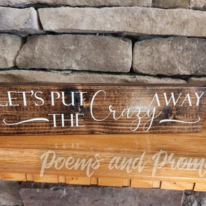 May include: A wooden sign with the text "Let's Put The Crazy Away" in white cursive lettering on a dark brown background.
