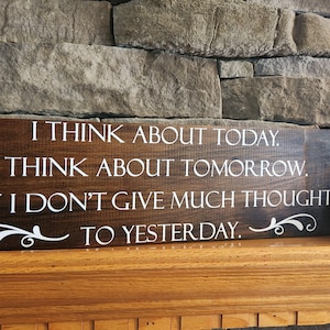 May include: A wooden sign with a brown stain and white lettering. The sign reads "I think about today. I think about tomorrow. But I don't give much thought to yesterday."
