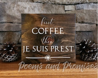 May include: A brown wooden sign with white text that reads "first coffee then je suis prest". The sign has a decorative floral design and the words "Poems and Promises" are printed at the bottom.