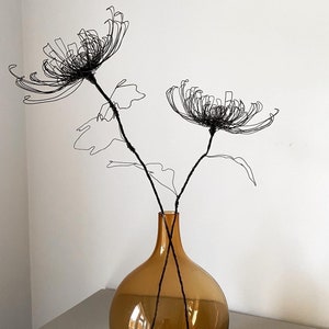 May include: Two black wire sculptures of chrysanthemums in a brown glass vase.