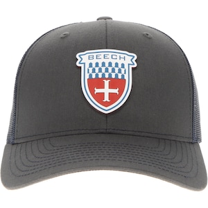 Könnte beinhalten: Eine anthrazitfarbene Baseballkappe mit Netzrücken und einem mittigen, schildförmigen Aufnäher. Der Aufnäher zeigt den Schriftzug BEECH in blauen Buchstaben über einem blau-weißen Karomuster und einem roten Bereich mit einem weißen Kreuz.