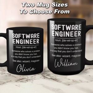 K&ouml;nnte beinhalten: Zwei schwarze Kaffeetassen mit wei&szlig;em Design. Die Tassen zeigen die Definition eines Softwareentwicklers mit den Worten "Software Engineer" und "noun. [de-vel-op-er]" oben. Die Tassen haben die Namen "Olivia" und "William" unten.