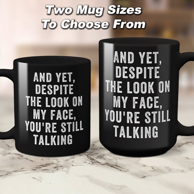 Pu&ograve; includere: Due tazze in ceramica nera con testo bianco. Le tazze riportano la frase "AND YET, DESPITE THE LOOK ON MY FACE, YOU'RE STILL TALKING". L'immagine include anche il testo "Two Mug Sizes To Choose From".